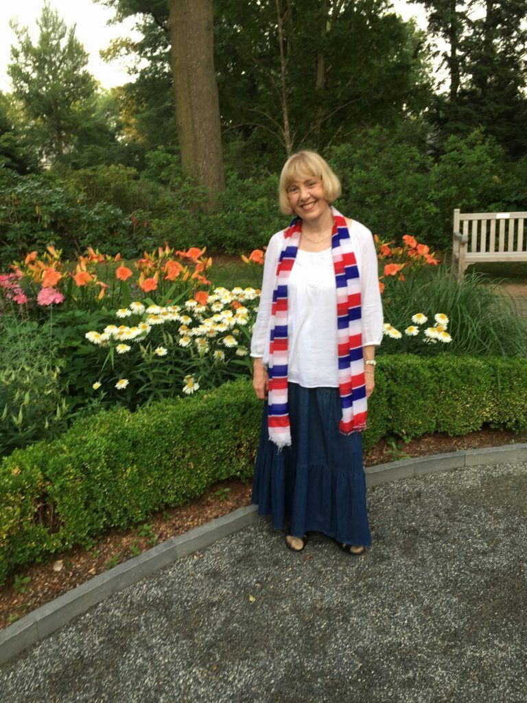 A woman wearing a red , white and blue scarf is standing in front of a garden.