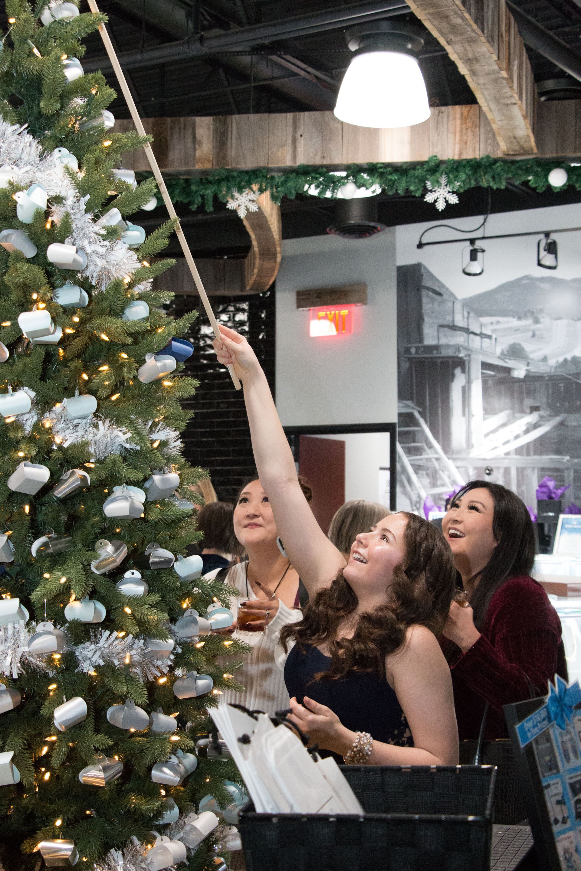 A group of three women decorating a Christmas tree indoors. 