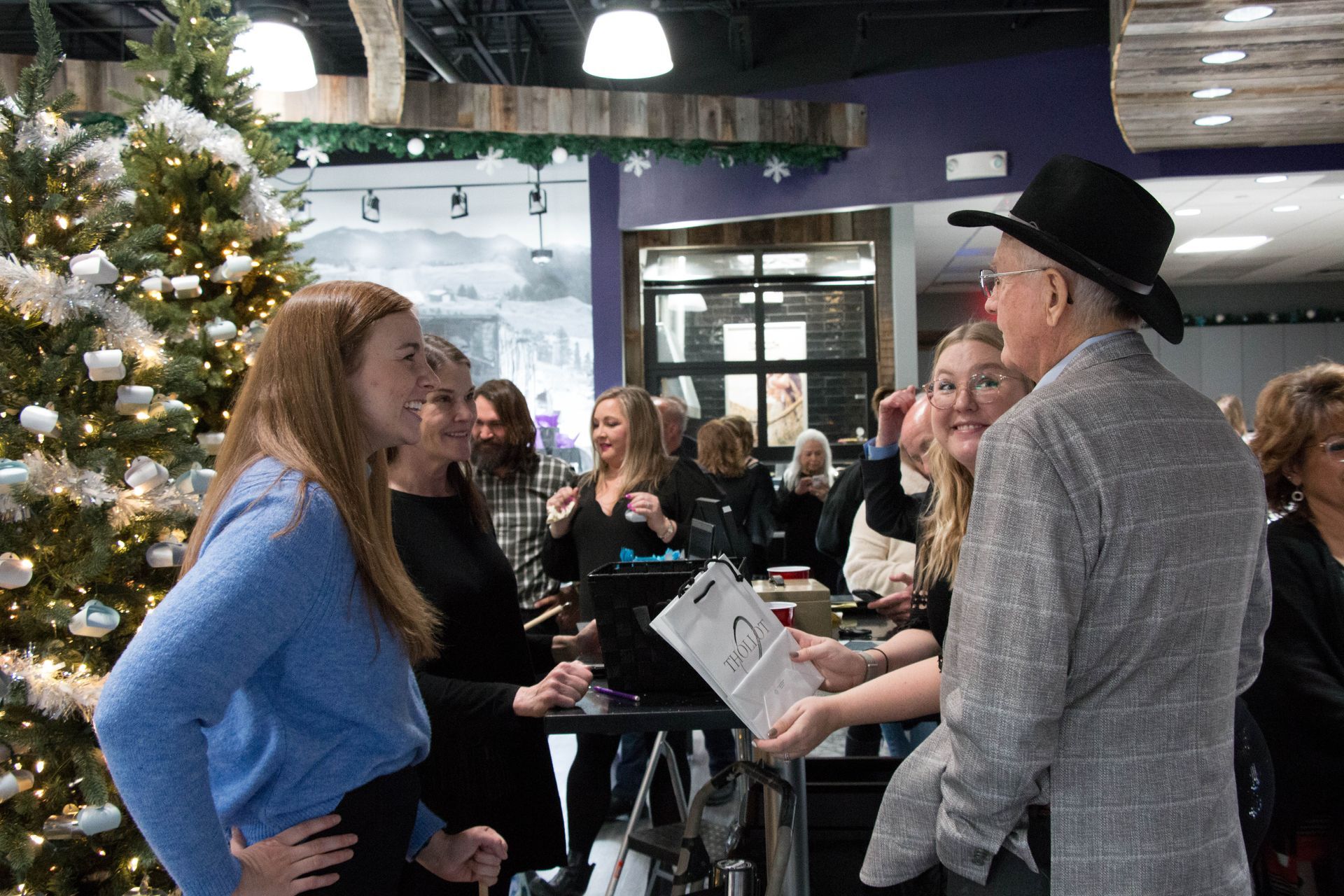 A group of people socializing inside a decorated venue with a Christmas tree. 