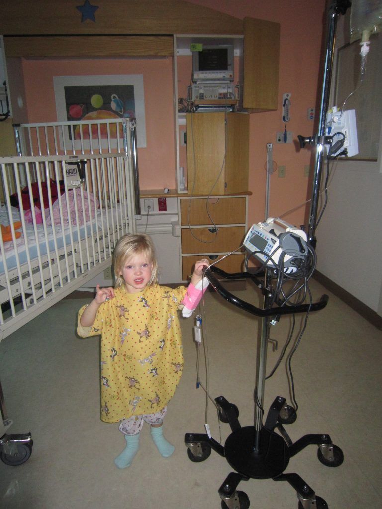 A little girl is standing in front of a medical device in a hospital room