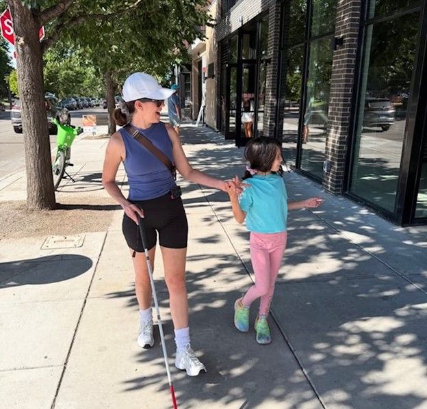 Woman walking down sidewalk with her daughter and holding a blind cane