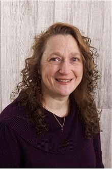 Author Monica Johnson with curly hair is smiling and wearing a purple sweater.