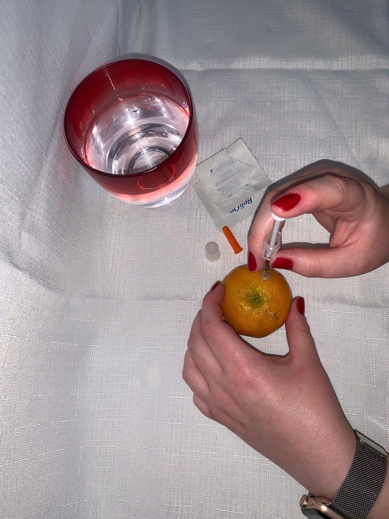 A woman is holding an orange in her hands next to a glass of water.