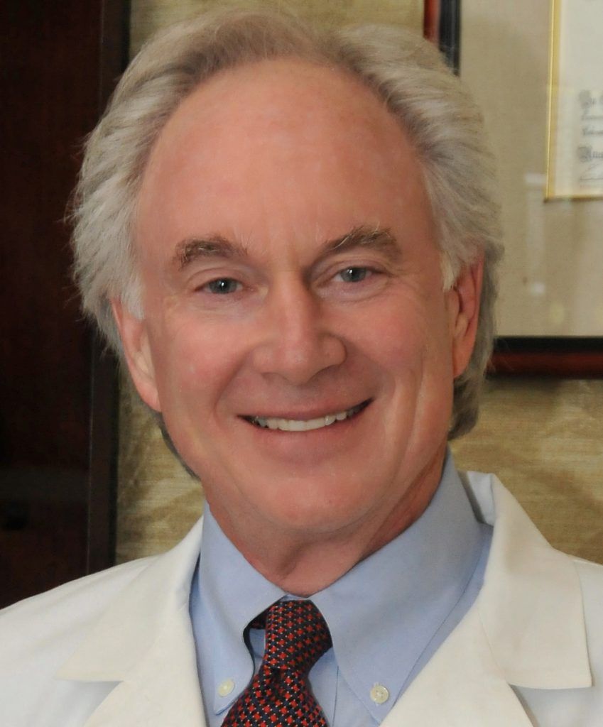A man in a white coat and tie smiles for the camera