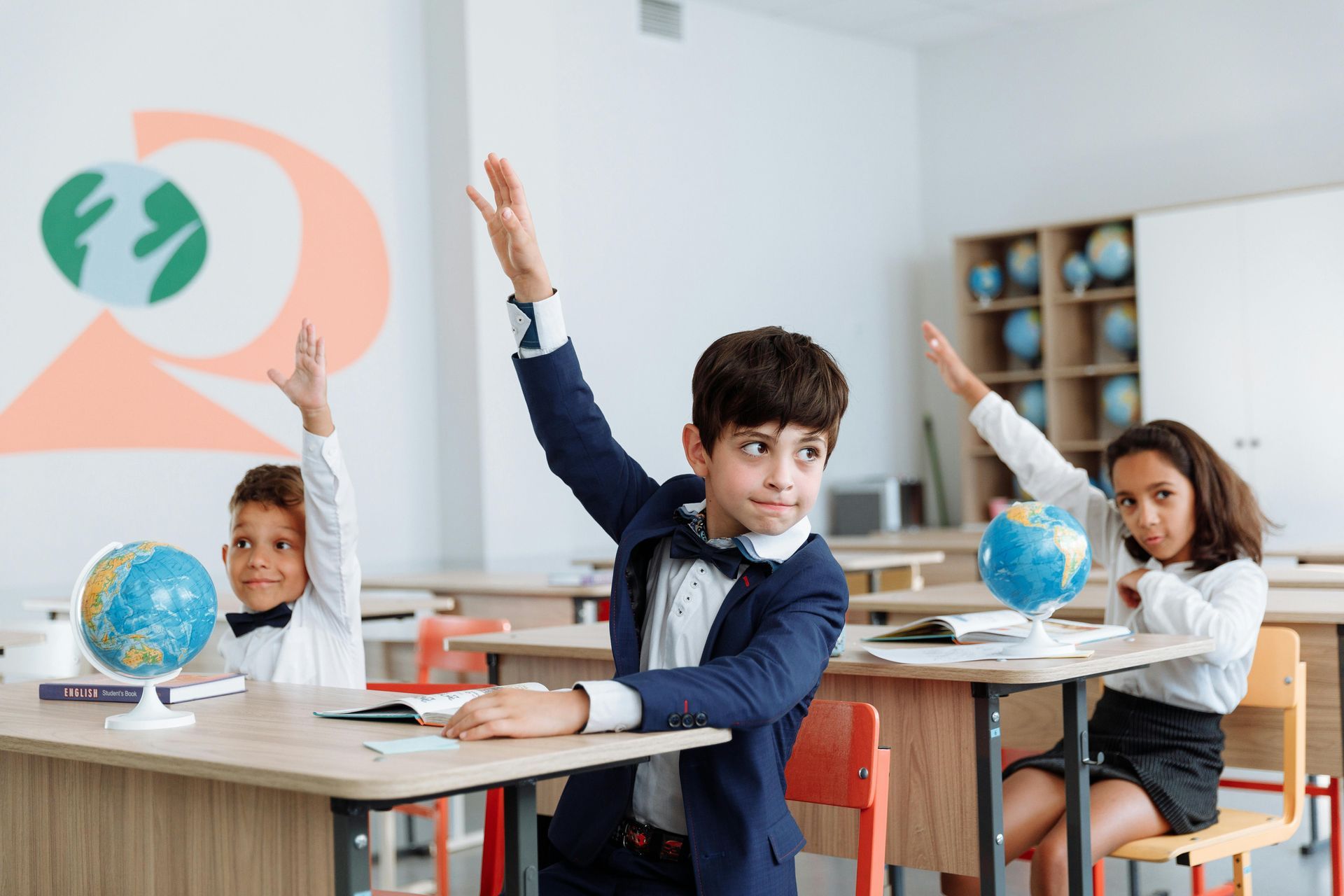 three young children in school room raising their hands to ask a question