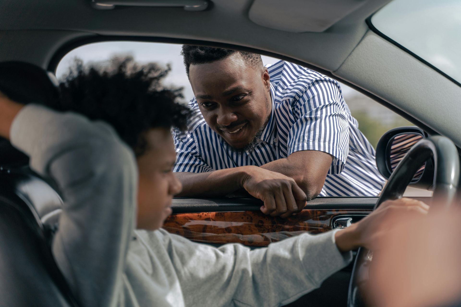 Father leaning in to the driver seat window to talk with his son.