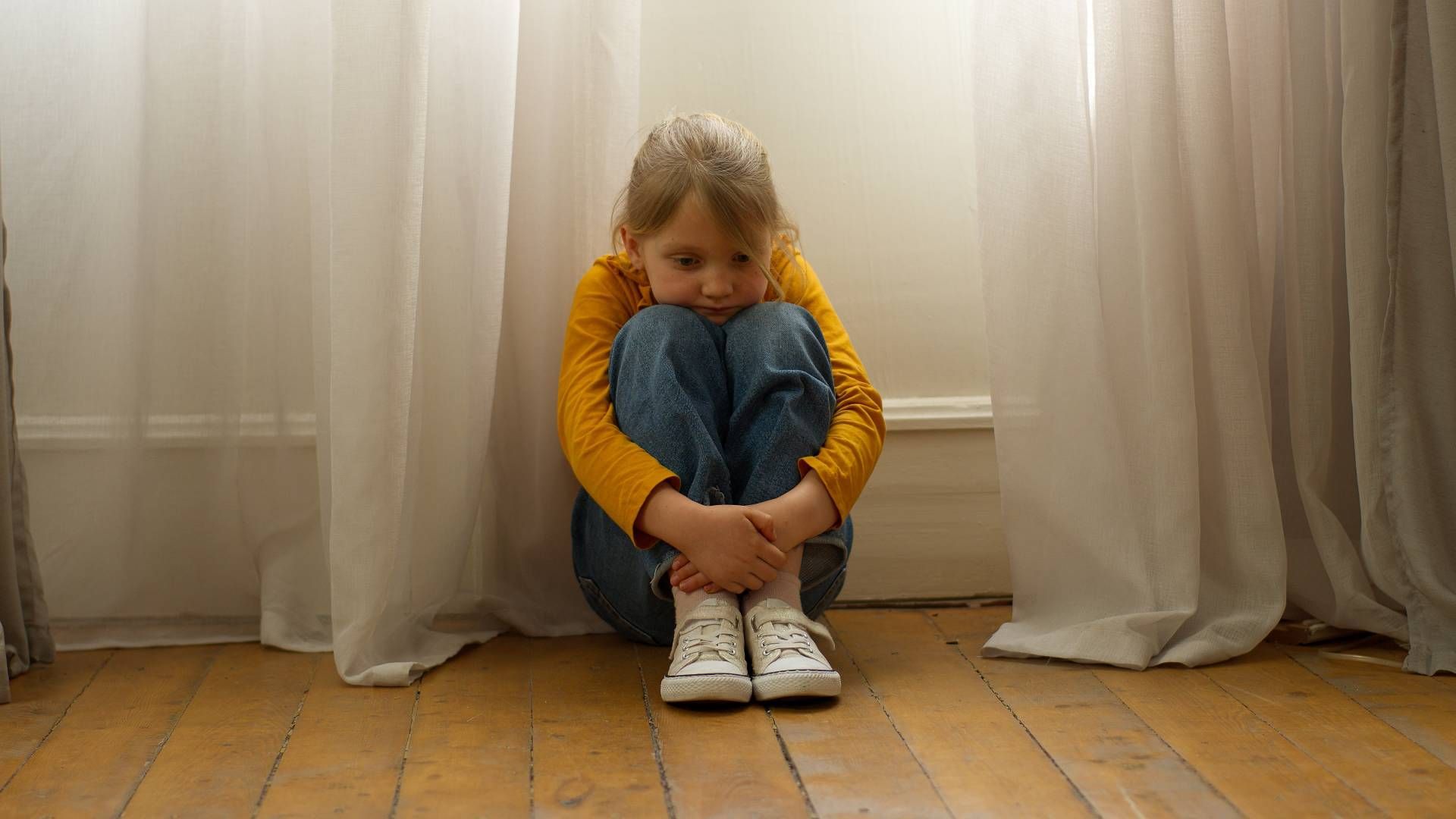 young girl on the floor hugging her legs and looking sad
