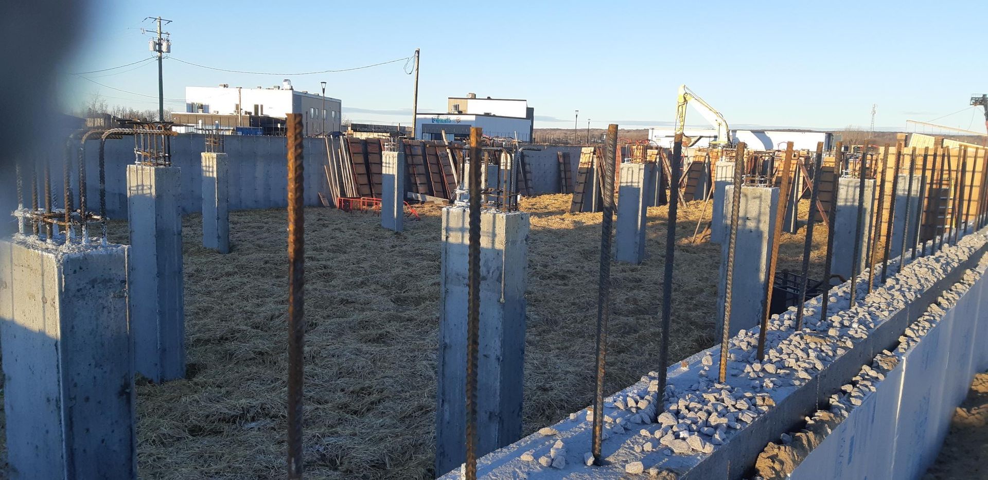 Chantier : piliers en béton, armatures et murs de fondation. Un ciel bleu dégagé.