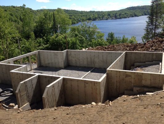 Fondations en béton d'un bâtiment sur une colline, surplombant un lac entouré d'arbres.