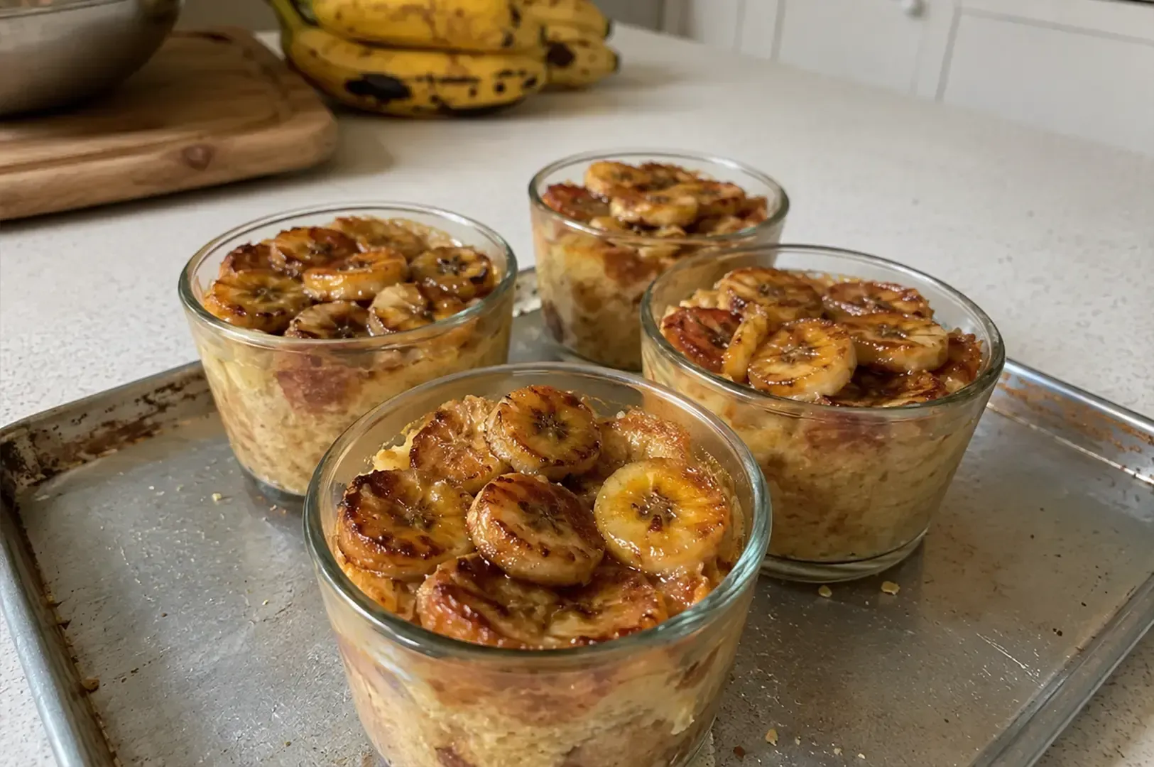 Four glasses of baked banana oatmeal topped with banana slices on a metal tray