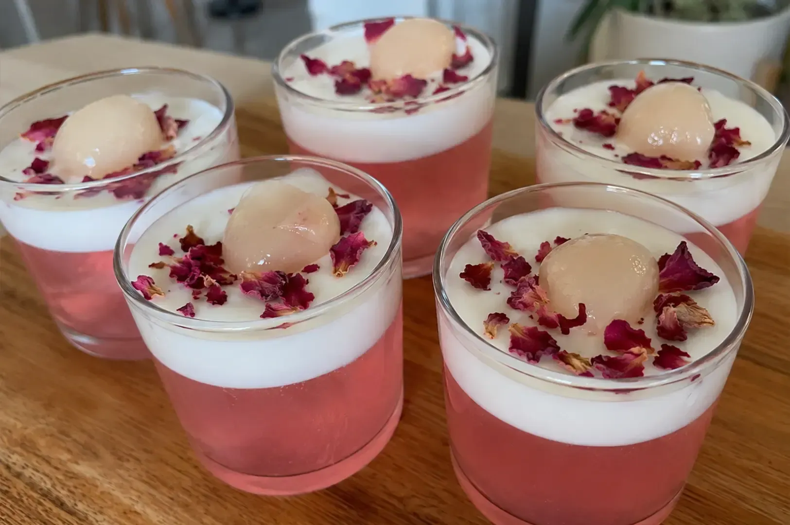 Four dessert cups with pink jelly, white cream, and a peach scoop topped with dried flowers.