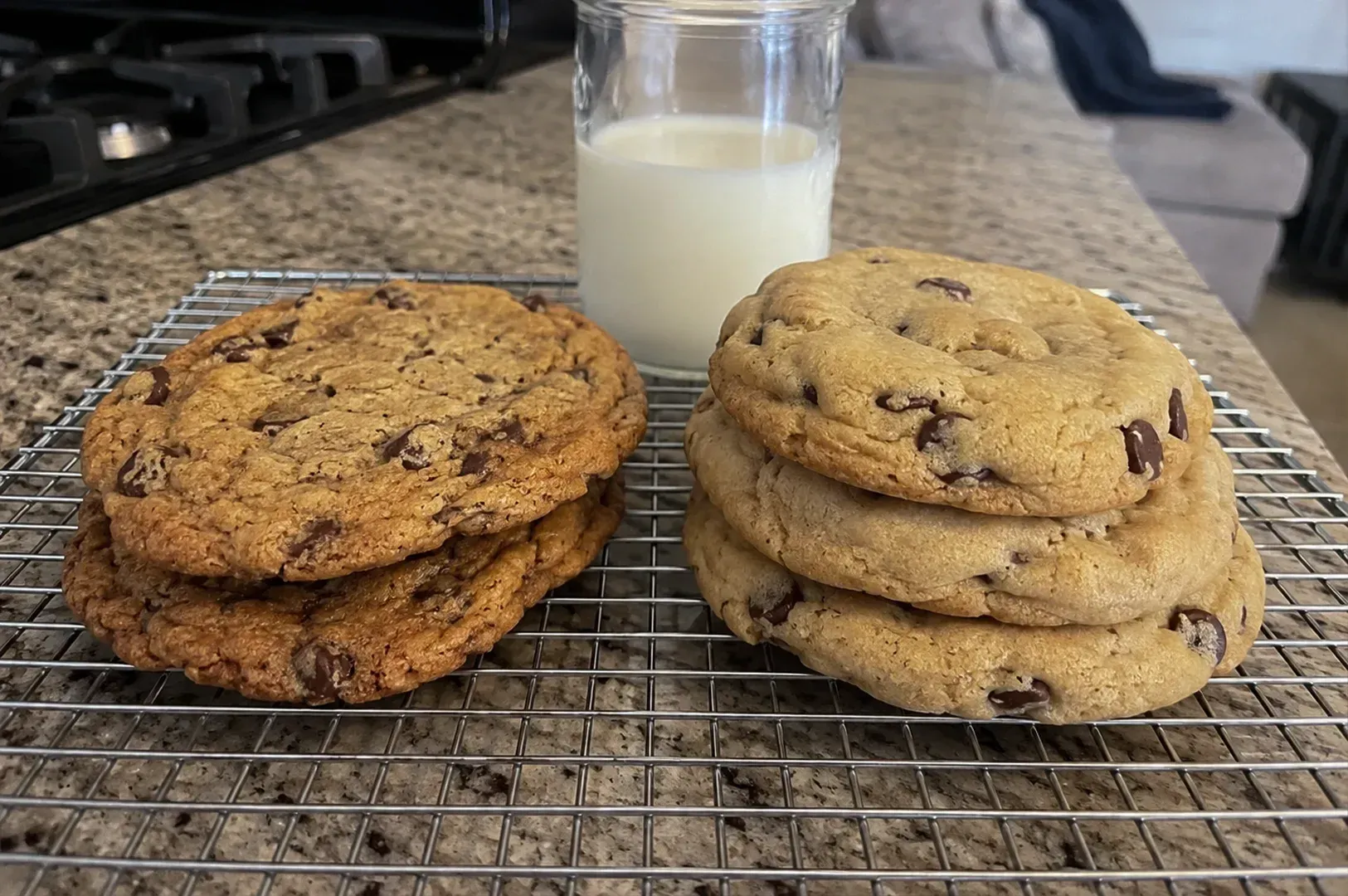 Two stacks of cookies on a cooling rack beside a glass of milk on a kitchen counter