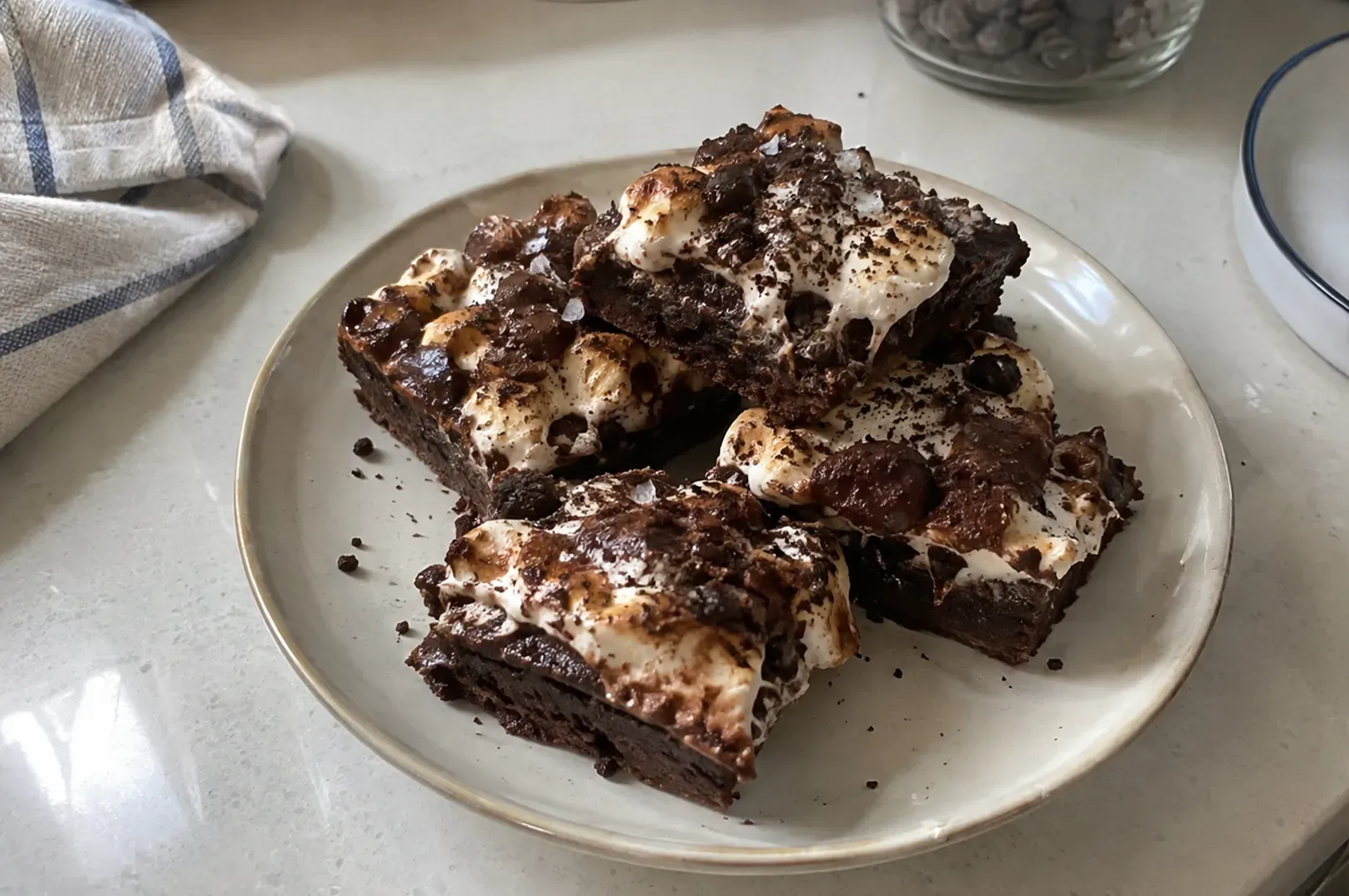 Plate of chocolate brownies topped with marshmallows and chocolate drizzle on a kitchen counter