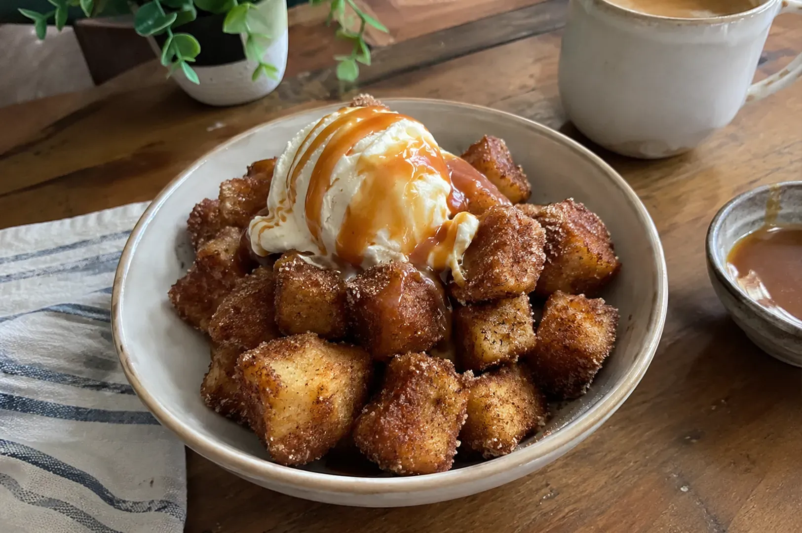 Dessert bowl with fried dough bites topped with vanilla ice cream and caramel sauce on a wooden table