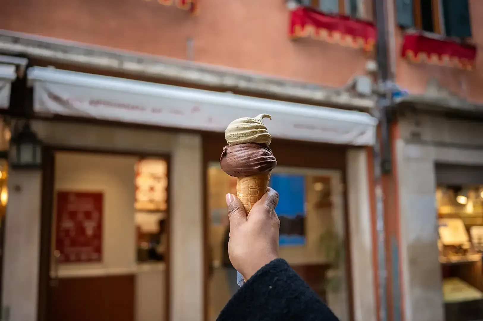 Hand holding a chocolate ice cream cone in front of a storefront