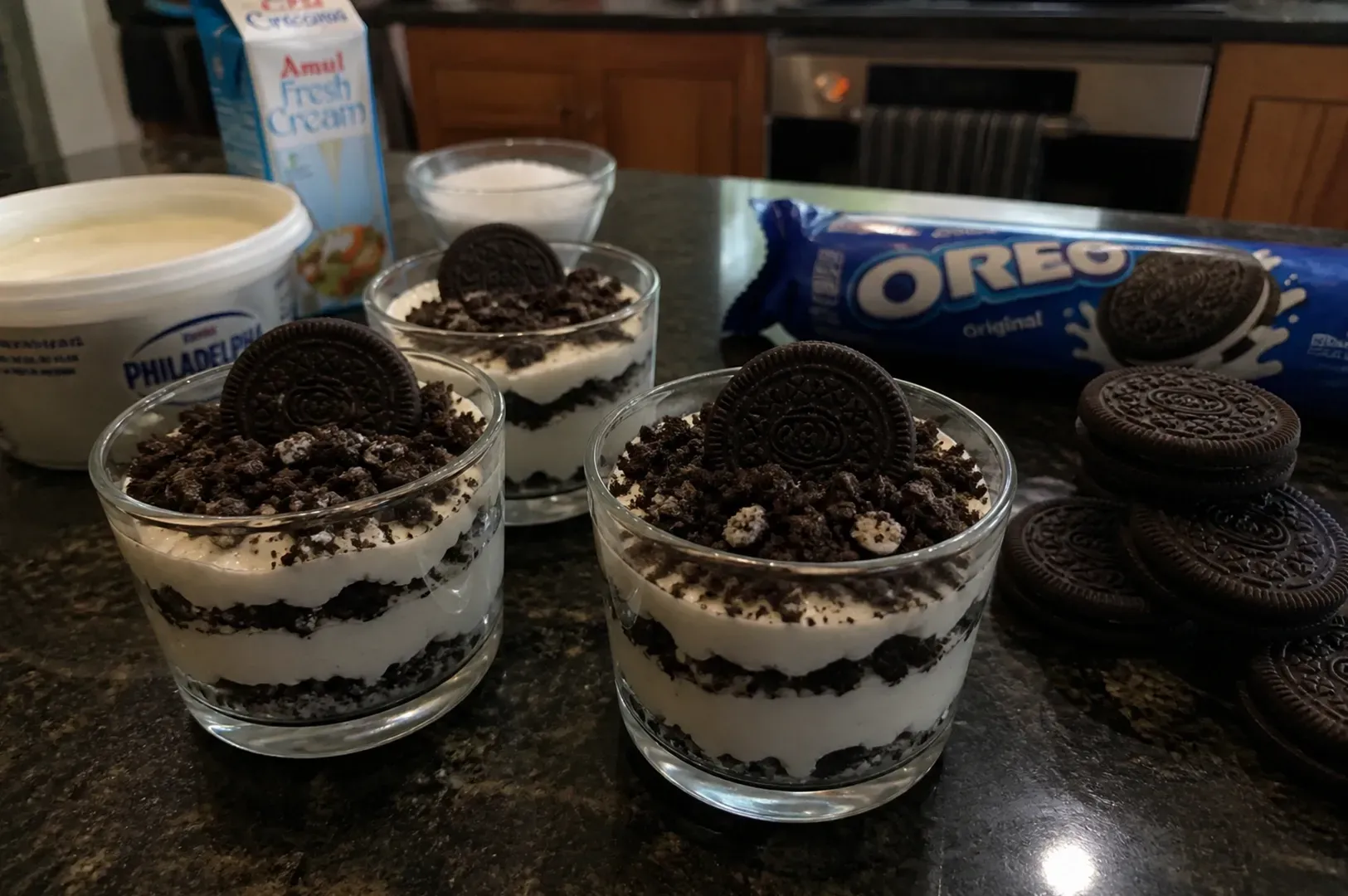 Chocolate Oreo dessert cups on a counter with an Oreo package and stacked cookies nearby