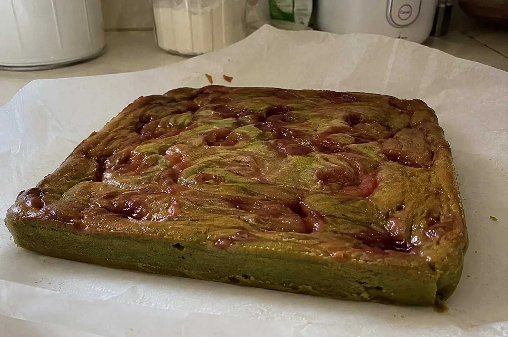 Green-glazed square dessert with swirled red topping on white parchment paper