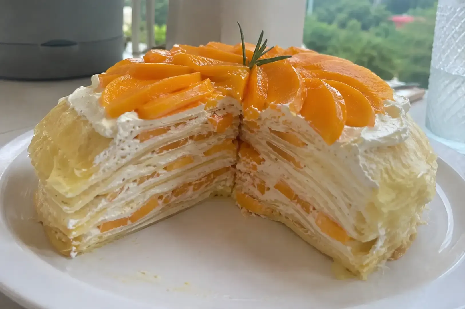 Slice of layered peach cream cake on a white plate, topped with peach slices and mint leaves