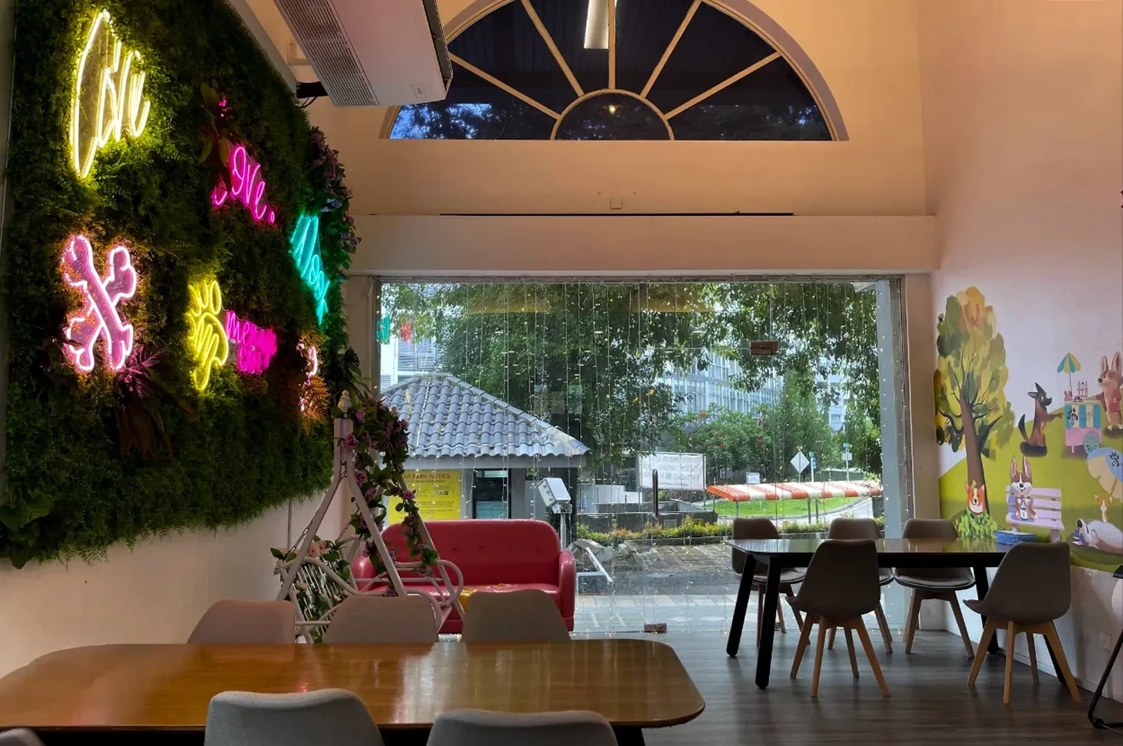 Cozy cafe interior with neon wall art, wooden tables, and large open windows facing a rainy outdoor patio