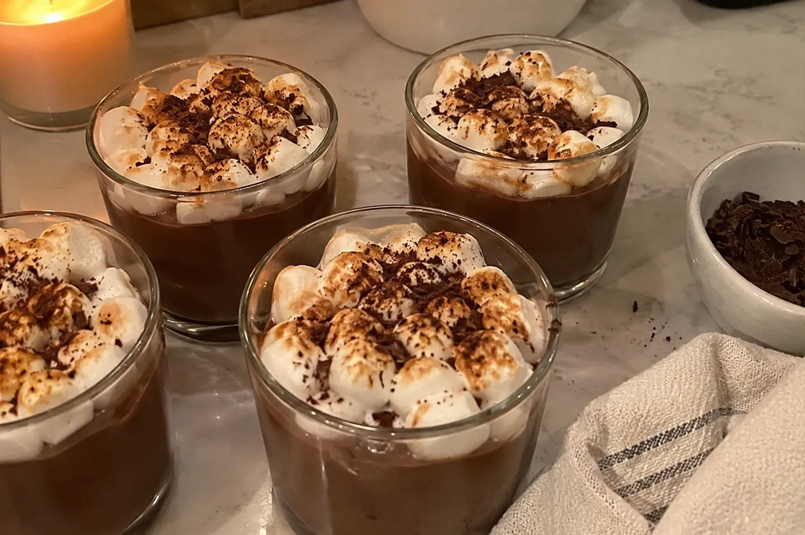 Chocolate dessert cups topped with whipped cream and cocoa on a kitchen counter