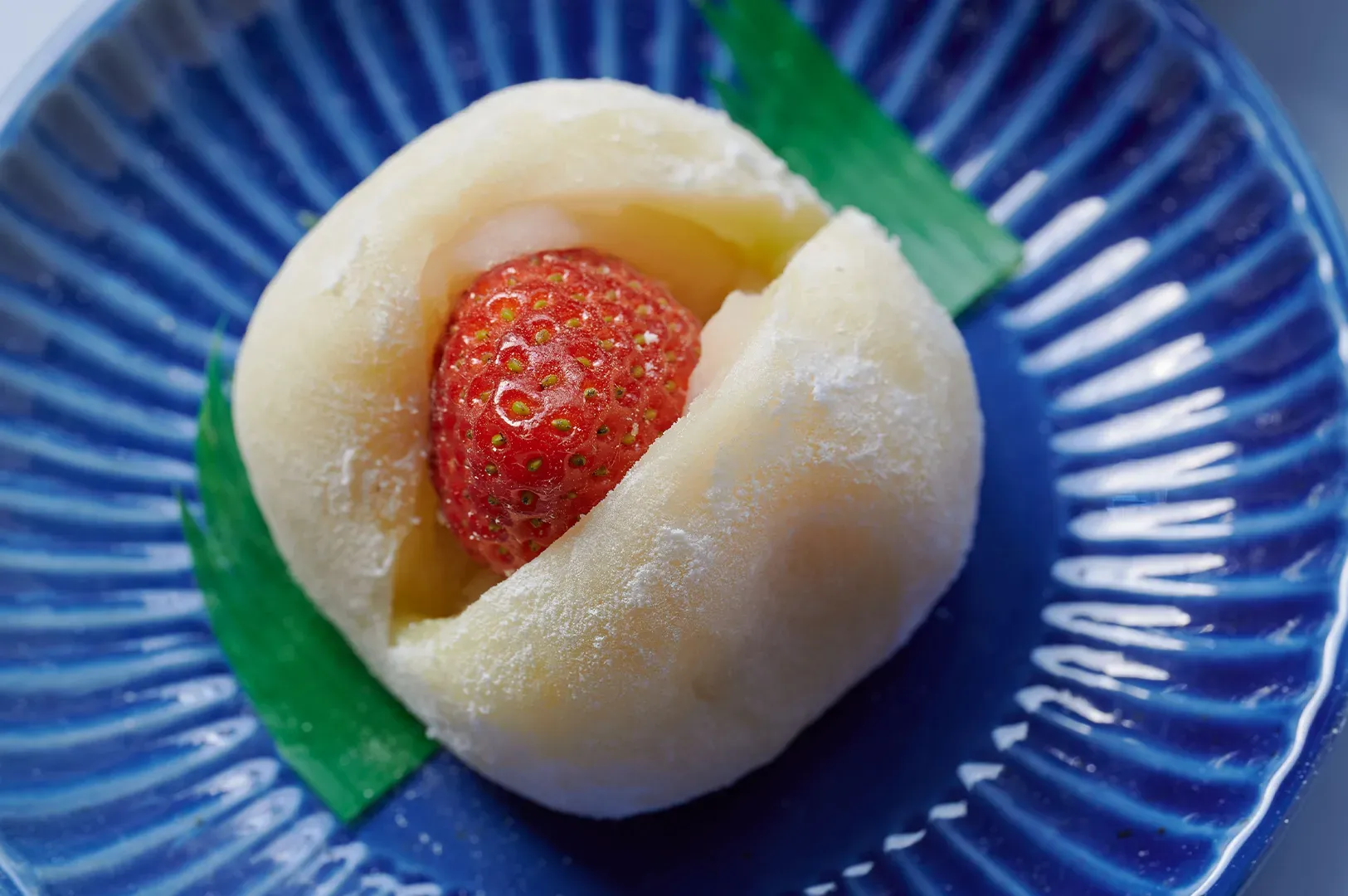 White mochi dessert with a red strawberry center on a blue plate