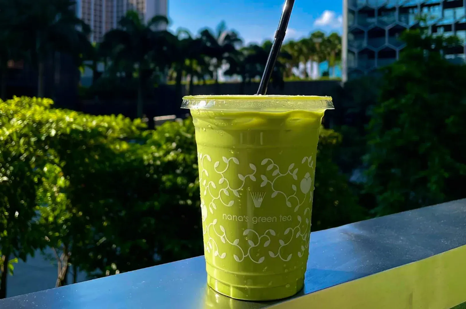 Green iced drink in a clear plastic cup with a straw on a sunlit outdoor table