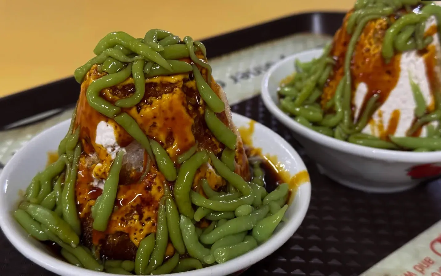 Two bowls of green noodles topped with sauce and rice cakes on a tray