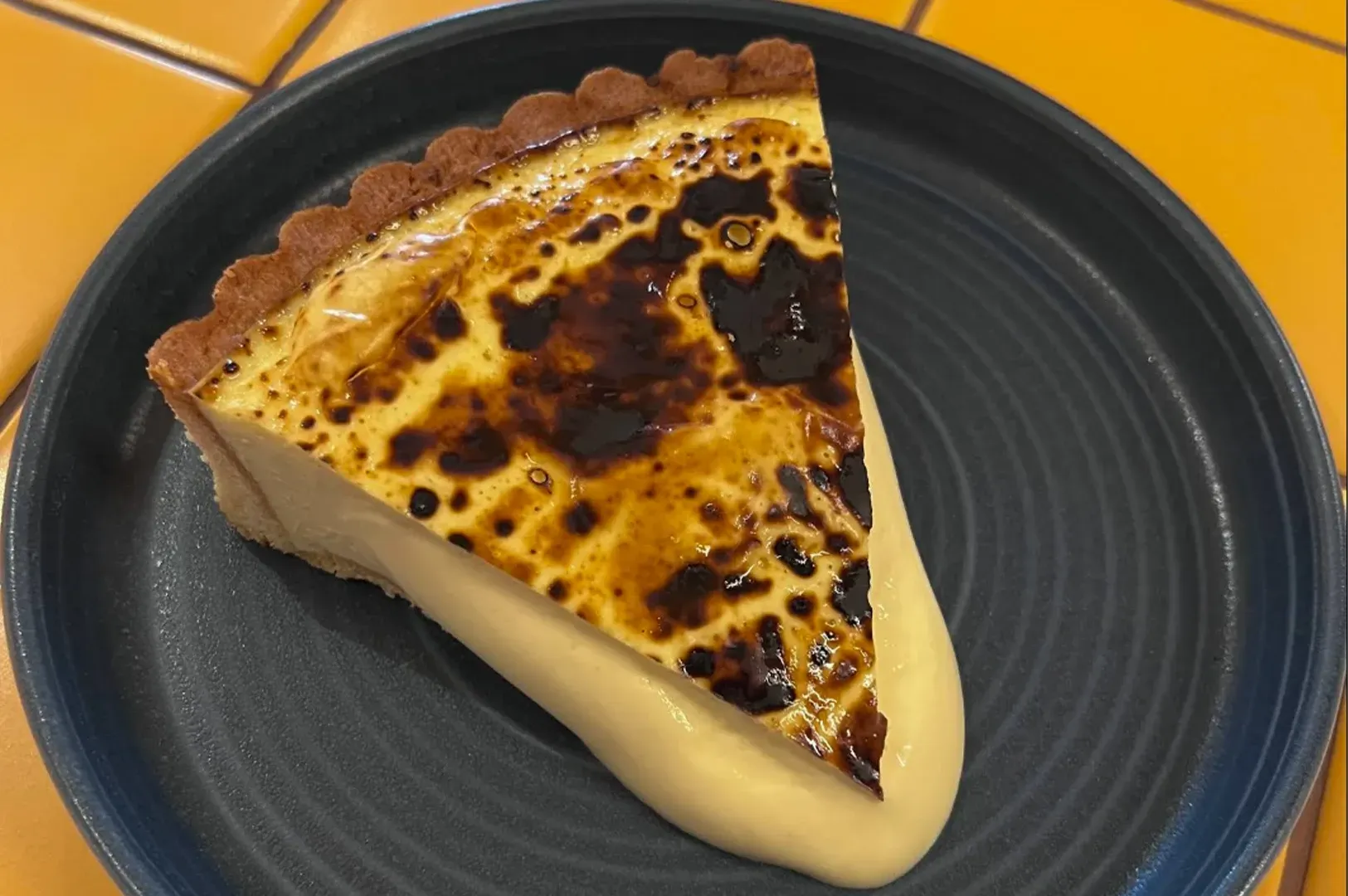 Slice of caramelized custard pie on a dark plate against an orange background