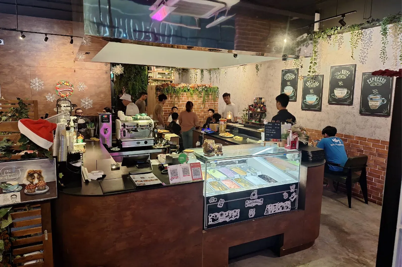 Bakery/café counter with glass dessert display, warm lighting, and several customers seated and browsing.