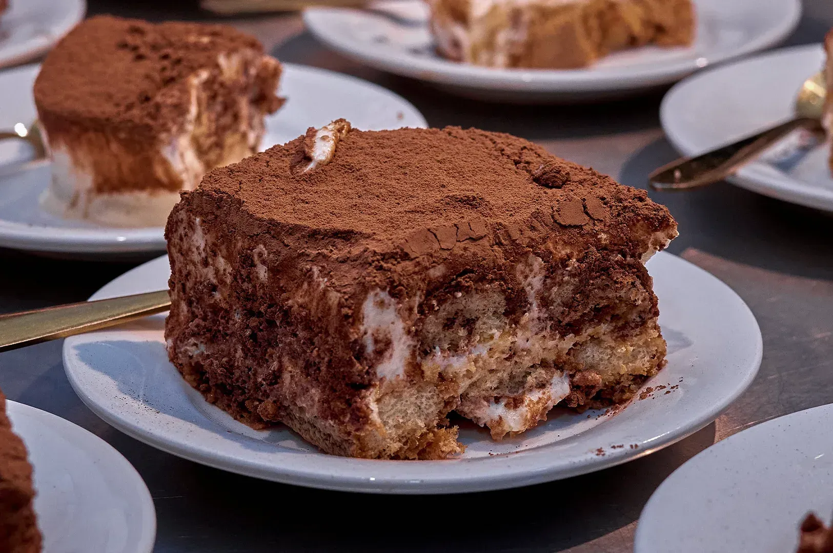 Slices of tiramisu on white plates, with cocoa-dusted tops and creamy layers visible