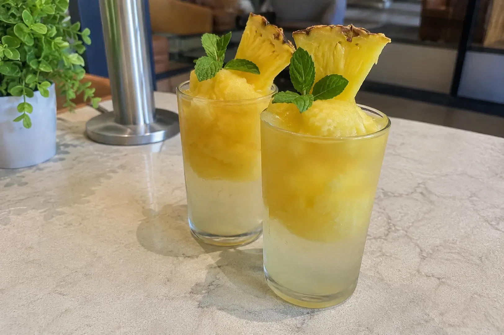 Two yellow tropical drinks with pineapple and mint on a table