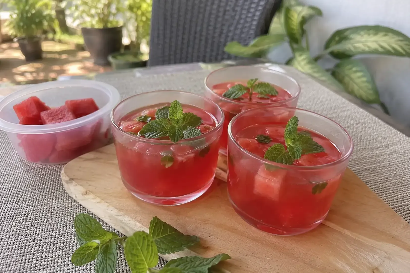 Glass cups of red strawberry dessert with mint on a wooden board, beside a bowl of strawberries outdoors