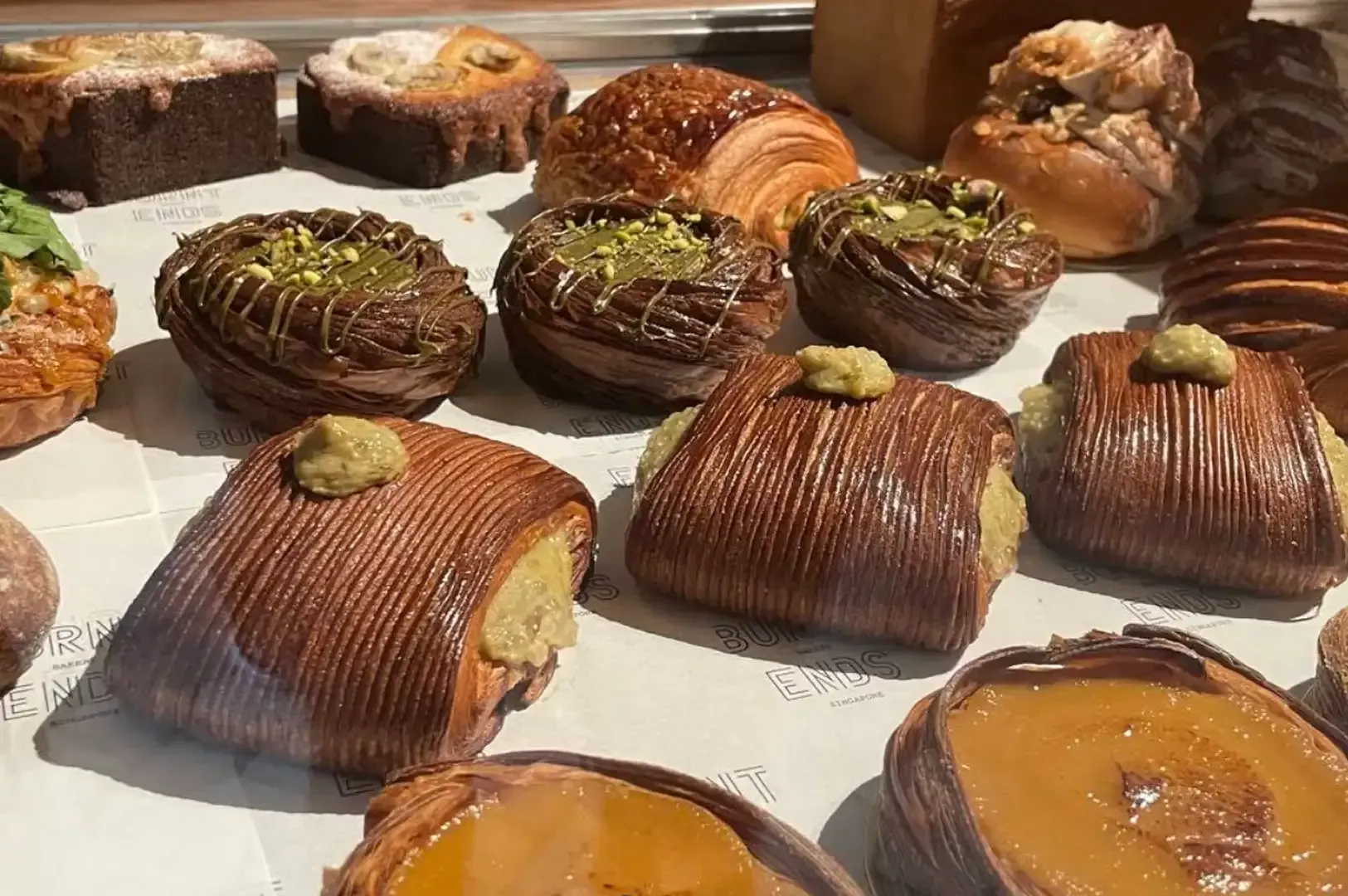 Tray of assorted pastries and tarts, including chocolate-covered squares with pistachio topping and fruit tarts.