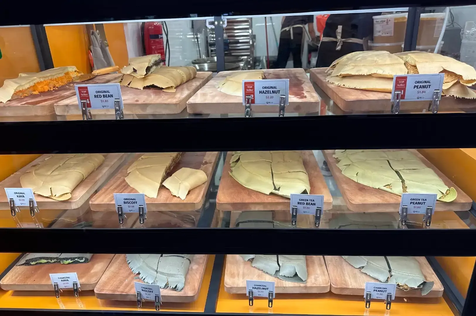 Bakery display case with assorted pastries and slices on trays, labeled with price tags.