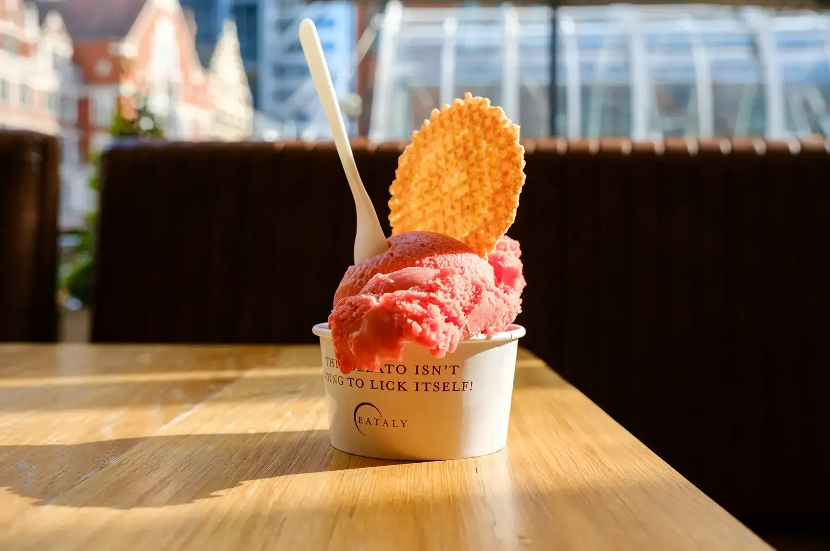 Pink shaved ice dessert in a small cup with a wafer on a wooden table in a café.