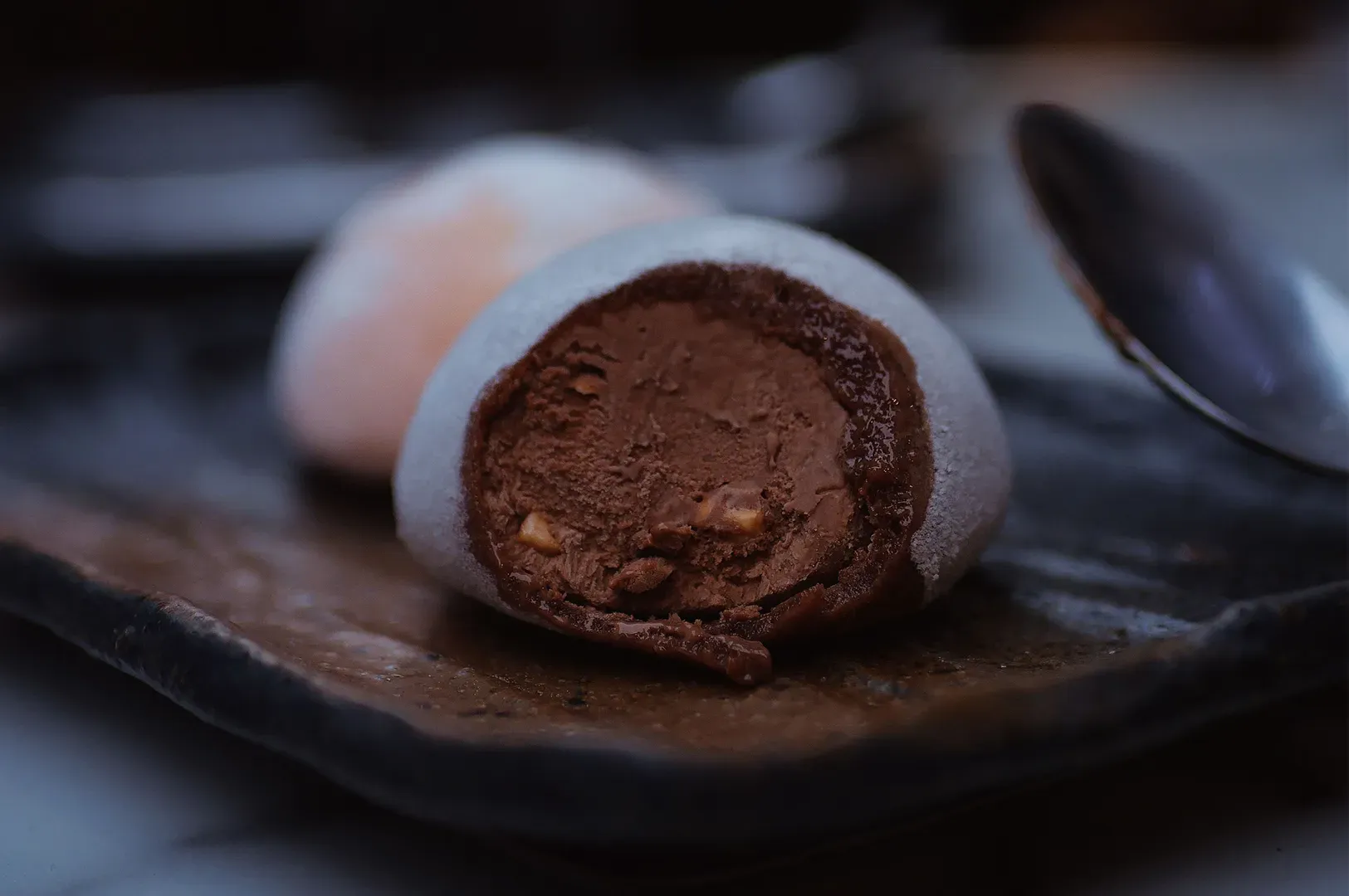 Chocolate truffle halves on a dark plate, with a spoon in the background