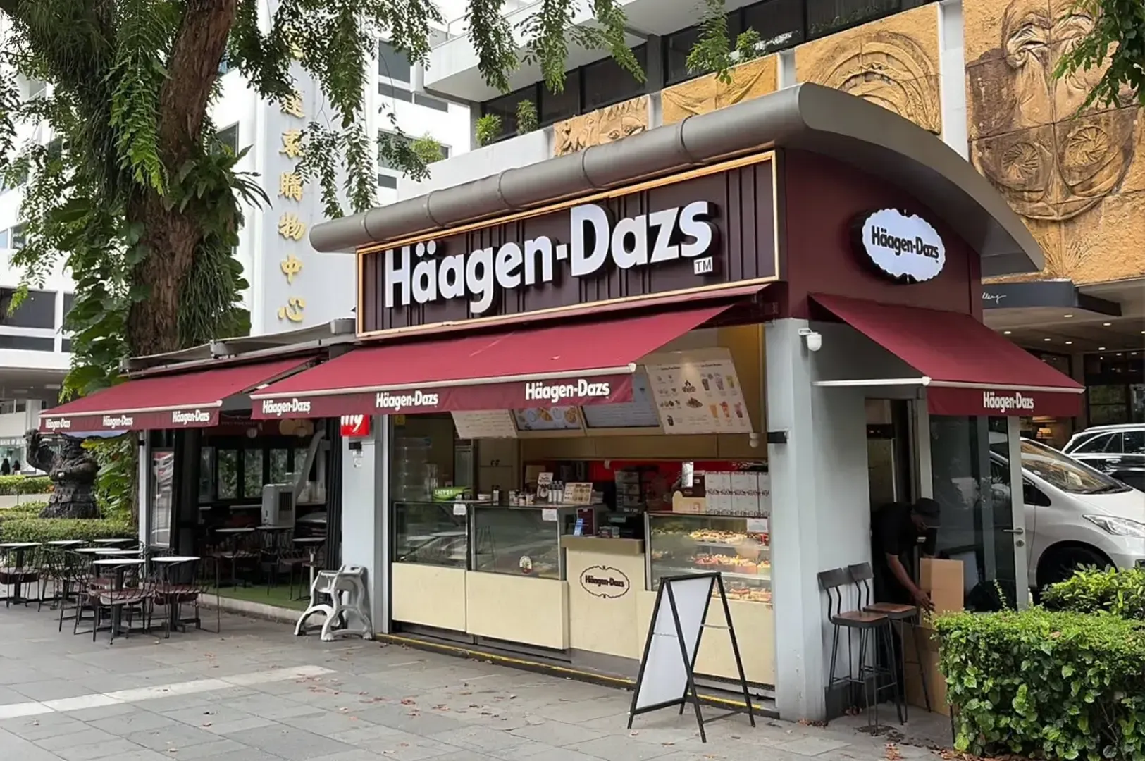 Häagen-Dazs ice cream shop with maroon awnings on a sidewalk, outdoor seating, and a menu board at the entrance