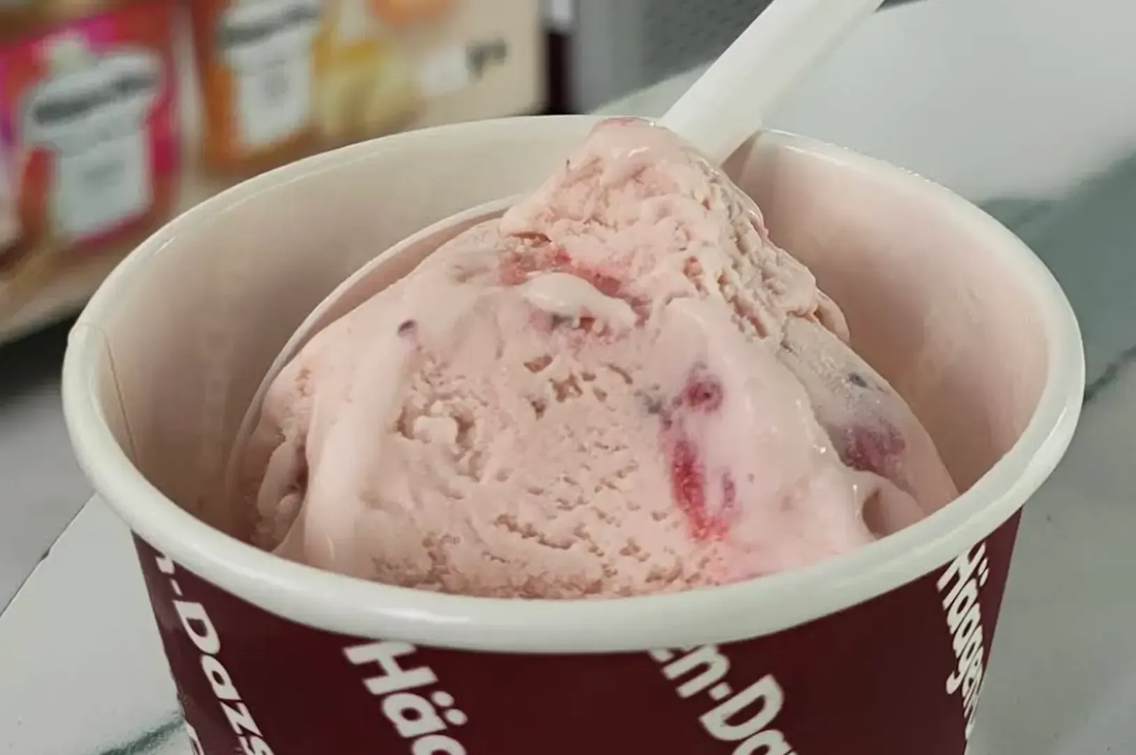 Pink strawberry ice cream in a paper cup with a white spoon