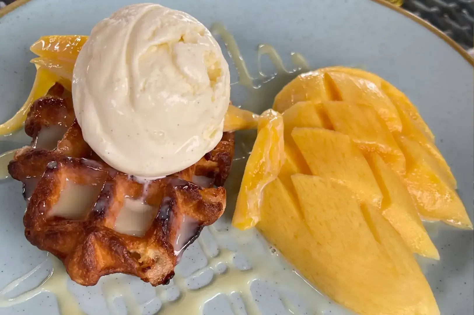 Waffle topped with vanilla ice cream and sliced mango on a gray plate