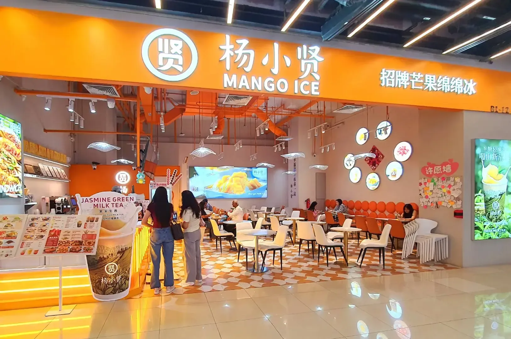 Mango Ice dessert shop with orange signage, glass display, and customers seated inside a bright mall food court