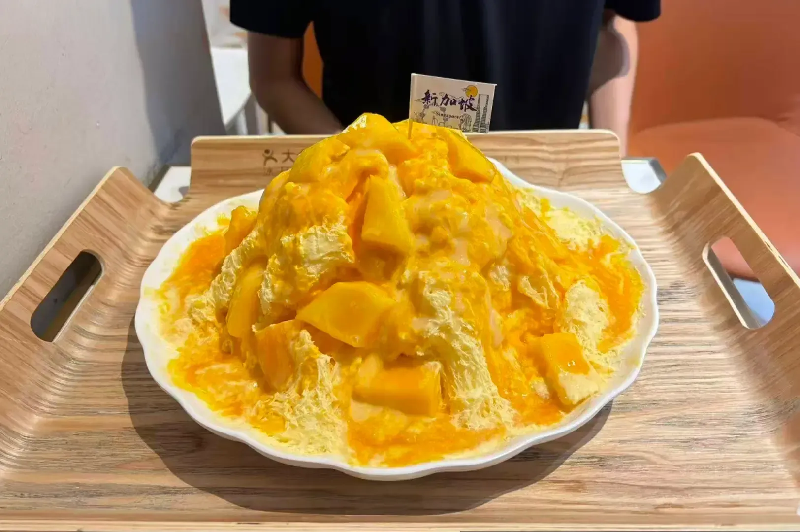 Tray of mango shaved ice with white ice cream, served on a wooden tray in a café setting.