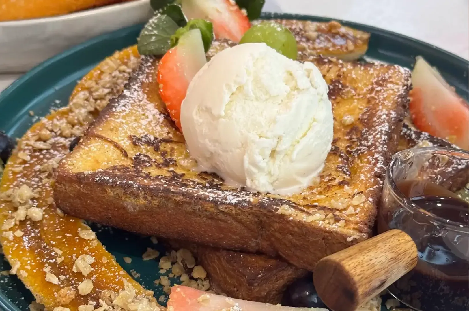 French toast topped with vanilla ice cream, cinnamon, and fruit on a teal plate