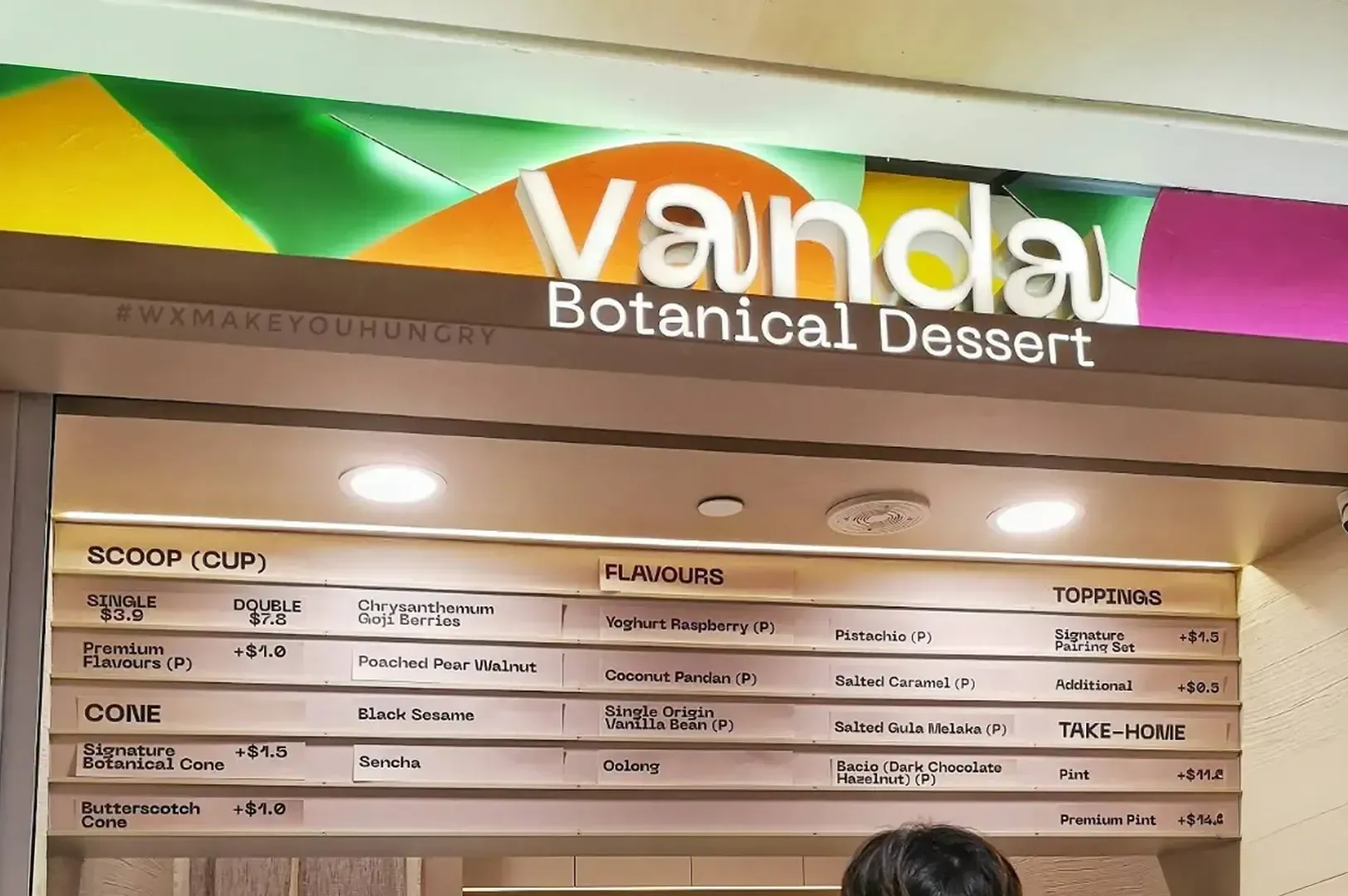 Menu board for Vounda Botanical Dessert with colorful green and yellow sign above flavor listings
