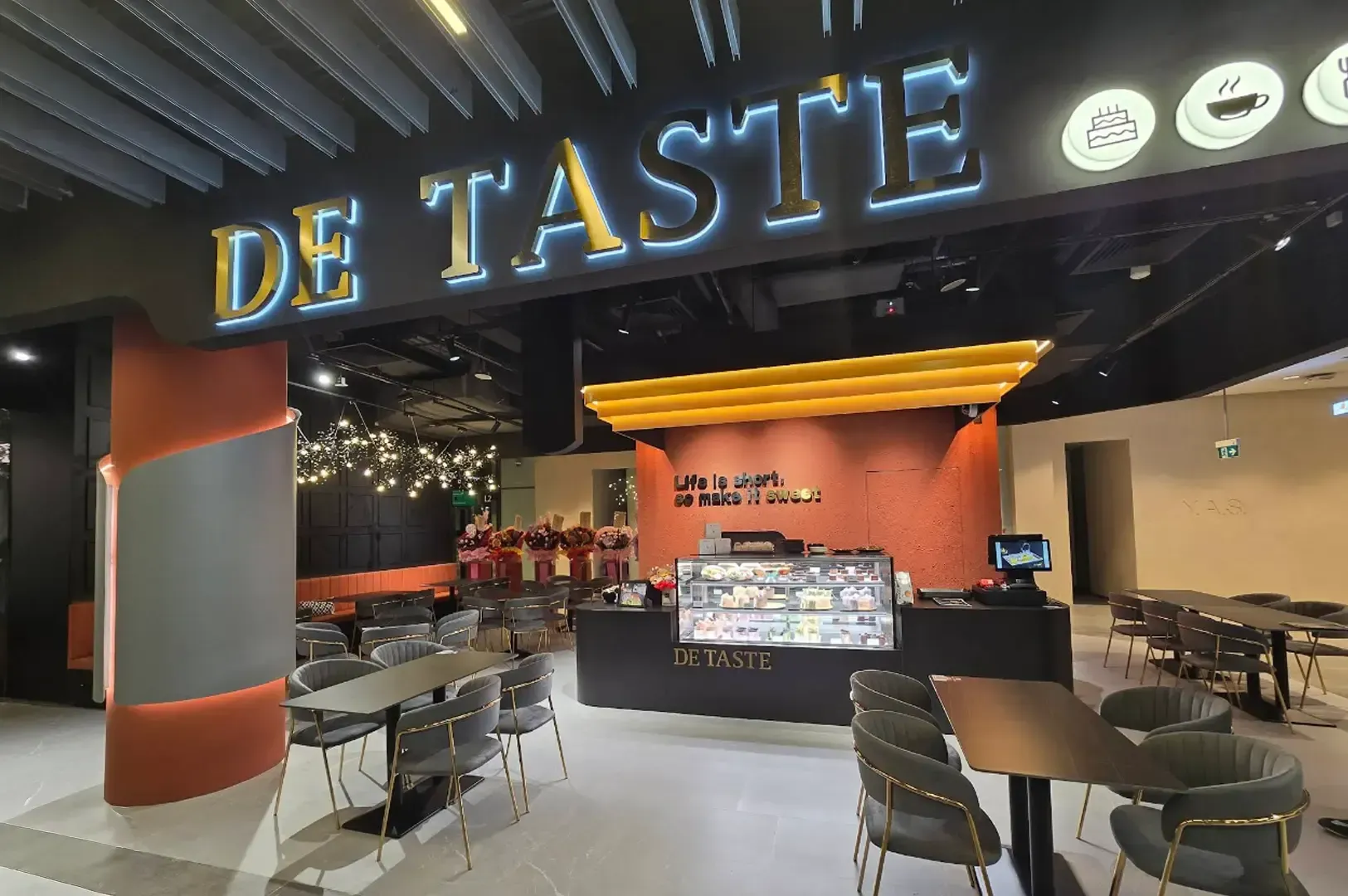 Interior of DE TASTIE restaurant with empty tables, chairs, and a lit orange counter area