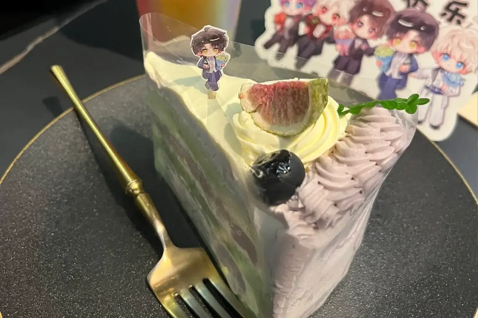 Slice of decorative cake on a black plate with a gold fork and anime character toppers in the background