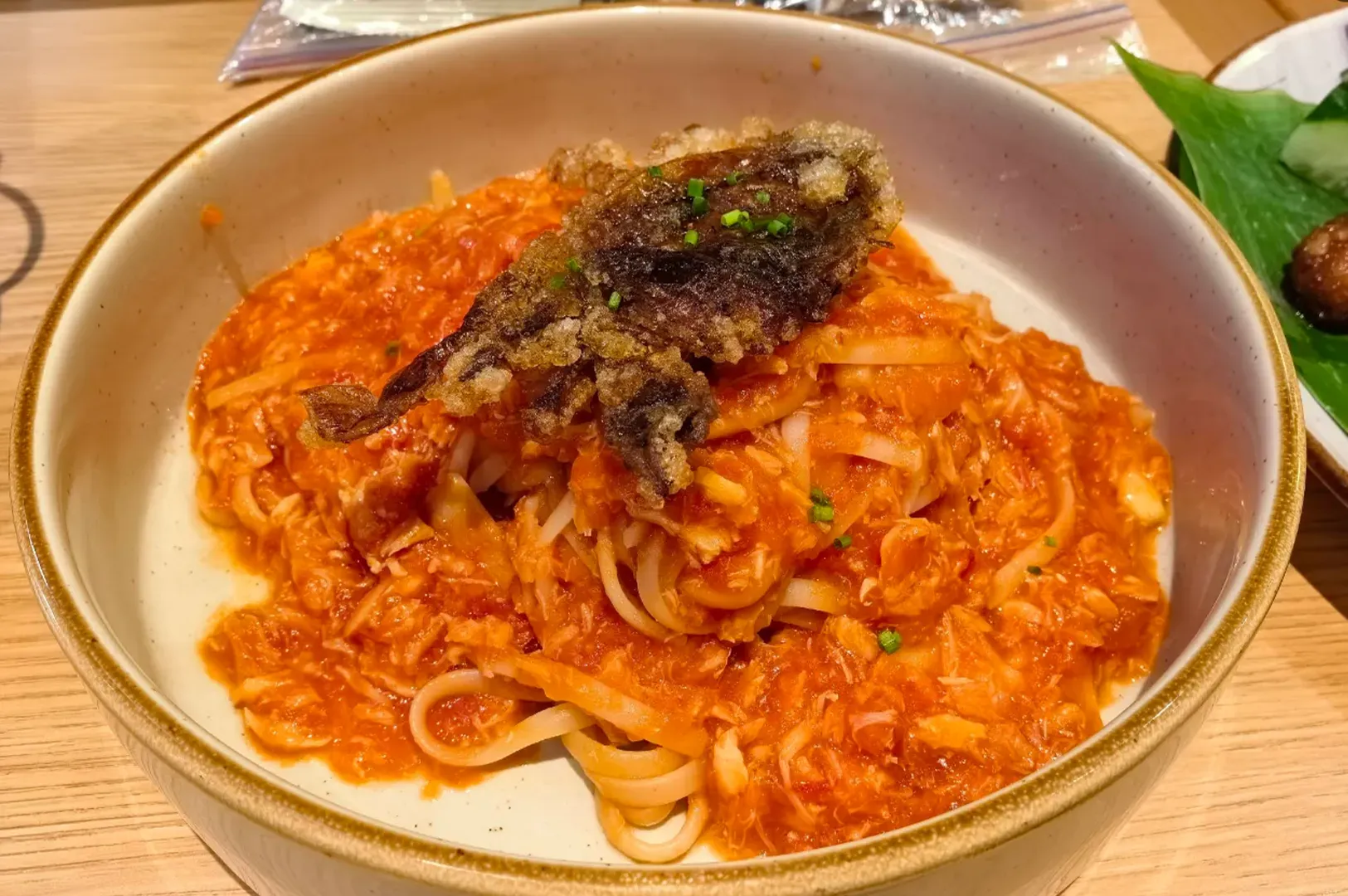 Bowl of noodles in red sauce topped with seaweed on a wooden table