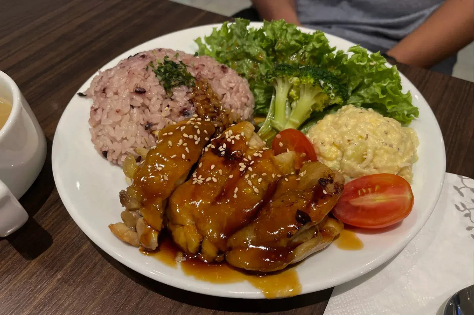 Plate of glazed chicken with rice, lettuce, potato salad, and cherry tomatoes on a table