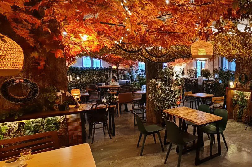 A cozy cafe interior designed like an indoor forest with orange autumn leaves covering the ceiling.