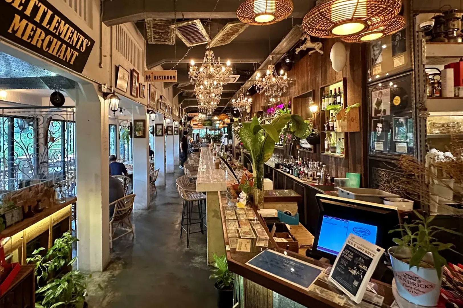 Cozy indoor market aisle with hanging lights, plants, and café tables, viewed from a laptop counter