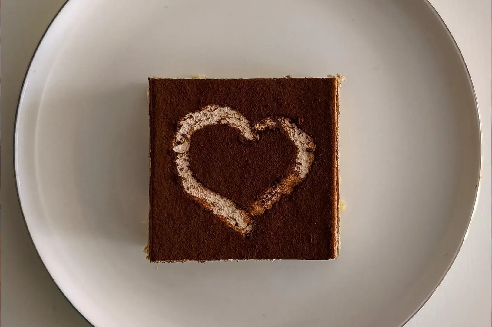 Chocolate dessert square on a white plate, topped with a heart made of powdered sugar.
